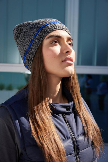 A coarse knitted beanie featuring grey and blue shades, worn by a model with long hair, against a modern backdrop.