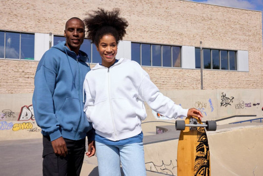 A blue oversized hooded jacket and a white oversized hooded jacket displayed on two individuals at a skate park.