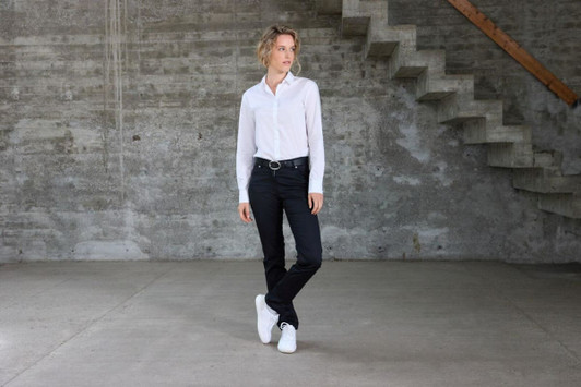 A white ladies shirt worn with black jeans and white sneakers, set against a concrete background with stairs.