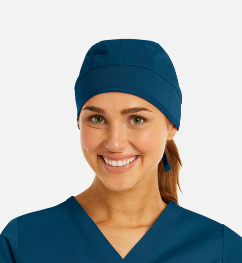 A unisex scrub cap in navy blue, worn by a smiling woman with a ponytail, featuring a logo.