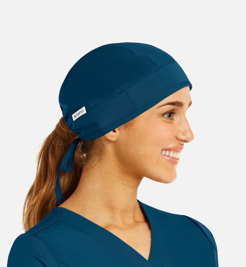A unisex scrub cap in navy blue, featuring a back tie and a logo patch, worn by a smiling individual.