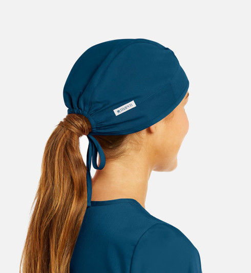 A unisex scrub cap in deep teal, featuring a tied design and a small branded label.