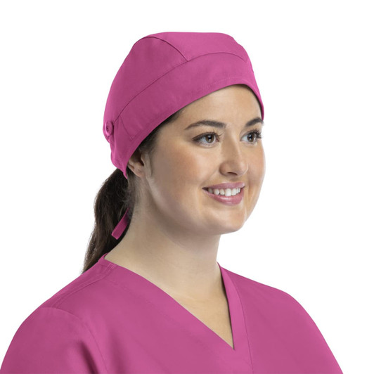 A pink unisex scrub cap with buttons, worn by a smiling woman in scrubs. The cap has a simple design and a back tie.
