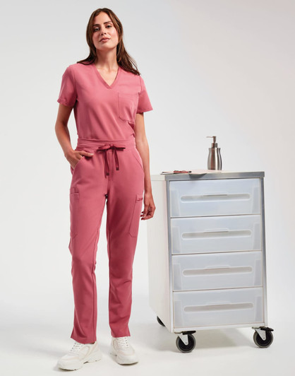 A woman wears pink cargo pants and a matching top, standing beside a mobile storage cart. The outfit features a drawstring waist.