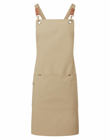 A tan cross-back bib apron featuring adjustable straps and a front pocket, with a logo on it.