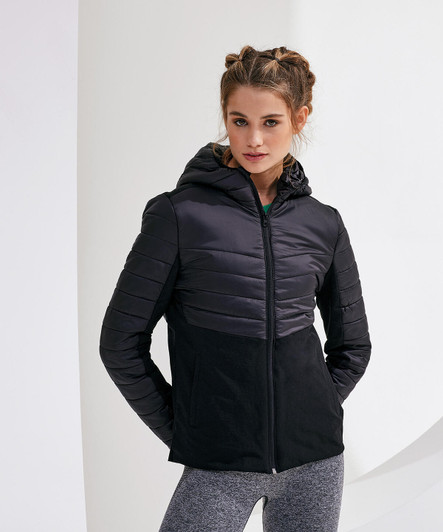 A woman wearing a black insulated hybrid jacket with a hood, featuring quilted panels and a sleek design.