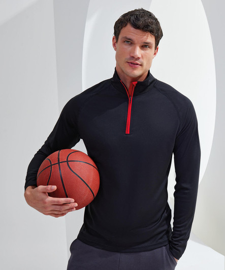 A model wearing a black long sleeve performance 1/4 zip top with a red zip, holding a basketball.