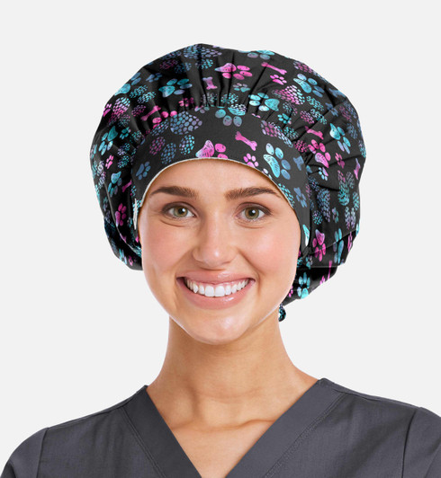 A bouffant cap featuring a black background with colourful floral and paw print patterns. The model is smiling.
