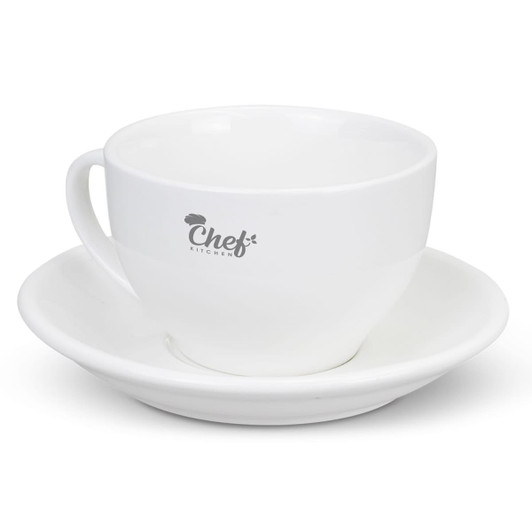 A white chai cup with a matching saucer, featuring a logo on the cup.