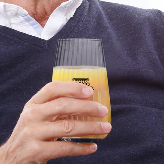 A glass tumbler with a ribbed design, partially filled with orange juice, held in a person's hand.