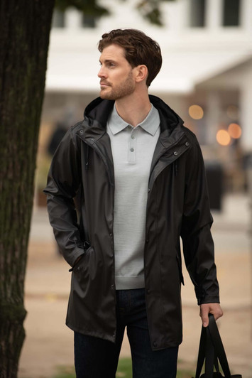 A sleek black unisex jacket with a hood, worn over a light grey polo, paired with dark jeans and a bag.