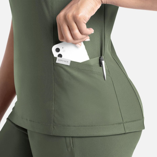 A green banded V-neck top featuring side pockets, one holding a phone and another with a pen. It has a logo.