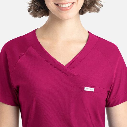 A model wears a vibrant magenta Embrace Luna Tuckable Y-Neck Top featuring a pocket and a logo.