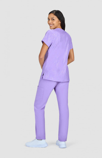 A woman wearing a purple printed top and matching purple pants, standing against a grey background.