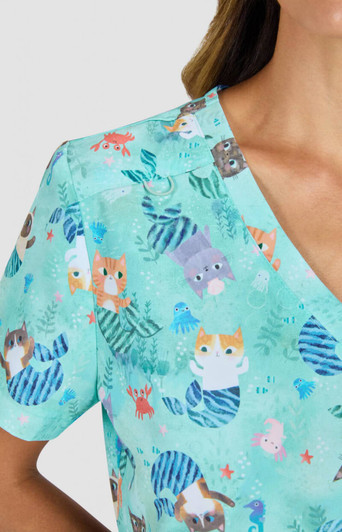 A short-sleeved top in a light teal with a playful animal print featuring cats and marine motifs. It has a branding logo.