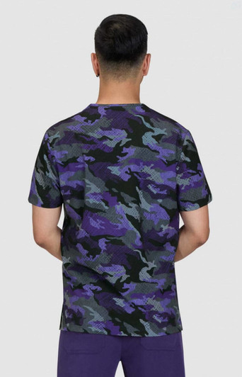A camouflage print t-shirt in shades of purple, green, and black, viewed from the back. The model is wearing purple pants.
