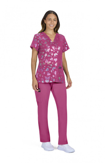 A woman wearing a pink scrub top with a heart pattern and matching scrub pants. The outfit includes a pocket detail.