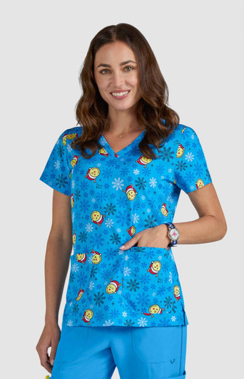 A blue scrub top with colorful smiley faces and floral patterns, featuring a pocket and a logo.