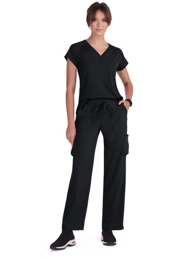 A person wearing a black top and black cargo pants, standing in a relaxed pose with a simple black logo visible.