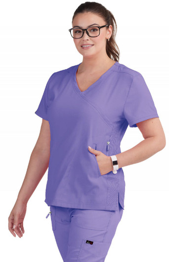 A woman wearing a purple scrub top with a V-neck and a side pocket, complemented by glasses and a watch.