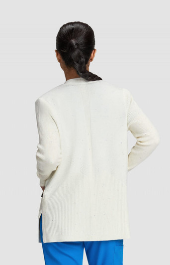 A woman stands with her back to the camera, wearing a white Kori Sweater and blue pants.