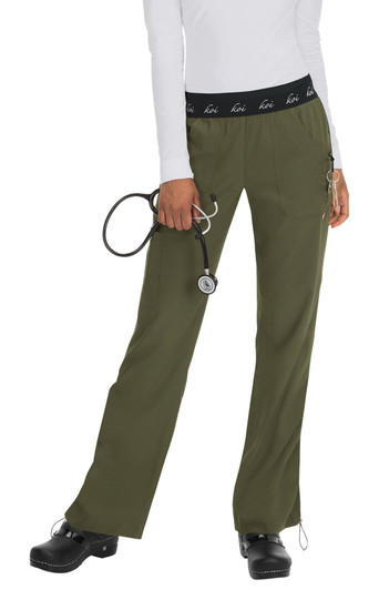 A pair of olive green scrubs with a black waistband, featuring a logo, held by a person with a stethoscope.