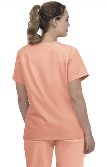 A woman wearing a peach-coloured medical scrub top, showing the back view with a simple design. The top has a logo.