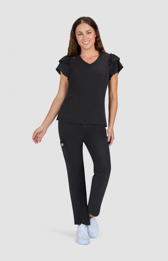 A woman is wearing a black top with ruffled sleeves and matching black pants, standing on a light grey background.