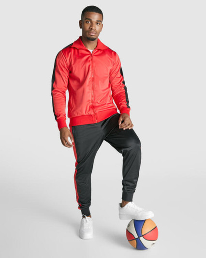 A track jacket in red with black accents, paired with matching black track pants. A basketball is on the ground.