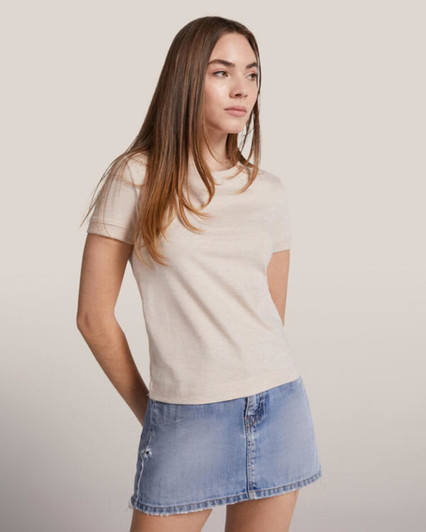 A light beige women's T-shirt with short sleeves, paired with a denim mini skirt. The shirt features a subtle logo.