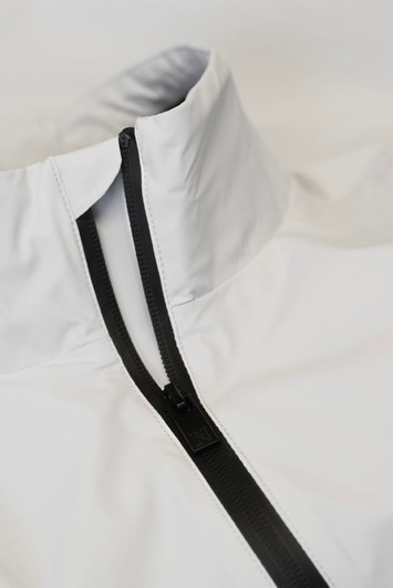 A white jacket with a high collar and a black zipper. Features a minimalistic design and has a logo.