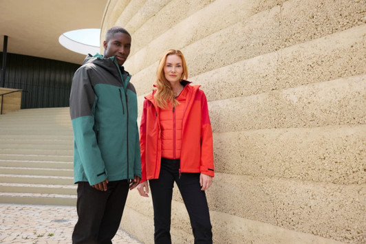 A red and grey women's 3-in-1 jacket and a teal and grey men's jacket displayed against a textured wall. Both feature logos.