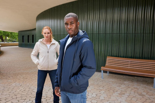 A ladies bomber jacket in light beige, worn by a model, alongside a model in a navy jacket. Both are outdoors.