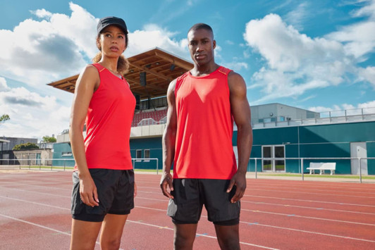 A red ladies' running tank, paired with a black running short, features one logo and is displayed outdoors on a track.
