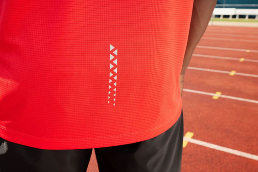A red men's running tank with a patterned detail and a logo, displayed on a person near a running track.