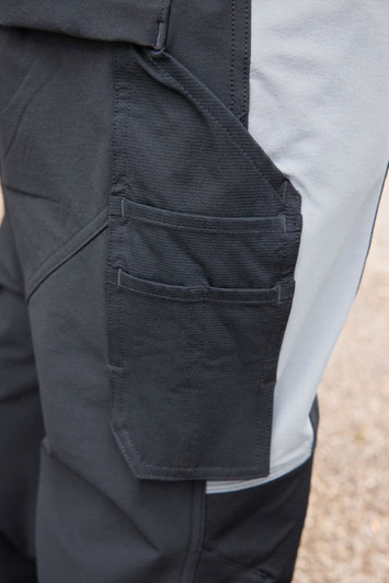 A close-up of a dark grey workwear softshell jacket featuring multiple pockets and a contrasting light grey side panel.