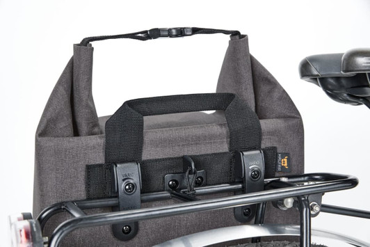 A grey cycle bike bag with a handle and fastening, attached to a bike rack. It has a sturdy design and a logo.