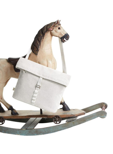 A cream coloured satchel bag with a flap and strap, displayed next to a rocking horse. The bag features a logo.