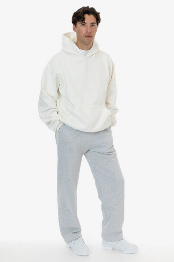 A model wearing a cream hoodie and grey straight leg heavy fleece pants. The pants feature a logo.