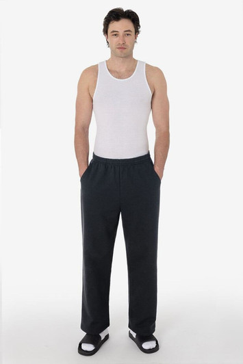 A man wearing a white tank top and black straight leg heavy fleece pants, standing with hands in pockets.