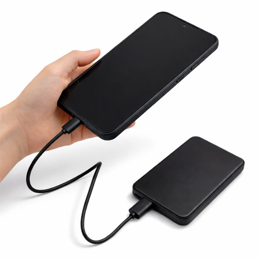A black solid state power bank with a charging cable connected, held in a hand.