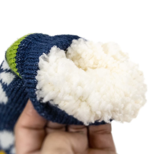 A hand holding a blue sock with a fluffy white interior and green detailing, featuring a decorative pattern.