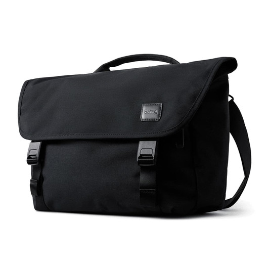 A black messenger bag featuring a flap closure, buckles, and a carrying handle, with a logo on the front.