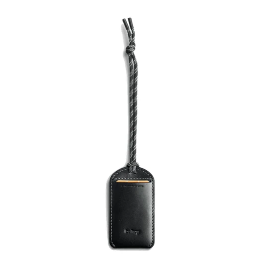 A black leather luggage tag features a braided strap and a logo. The design is sleek and minimalist.