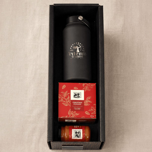 A black drink bottle, a red box of Christmas pudding, and a jar of sauce, all in a black hamper.