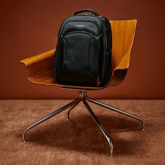 A black Samsonite Xenon 3.0 Backpack rests on a wooden chair with a chrome base.