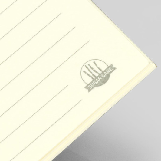 A soft cover notebook with lined pages in a pale yellow colour, featuring a logo in the bottom corner.