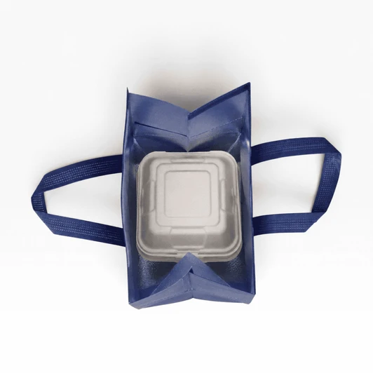 A navy insulated reusable bag with two handles, containing a square white food container inside. It has a logo on the exterior.