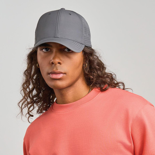 A grey cap worn by a model with curly hair, paired with a pink sweatshirt. The cap features a logo.