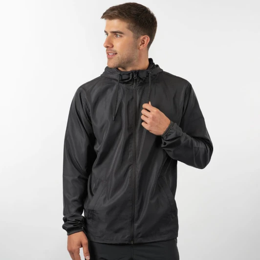 A man wearing a lightweight black windbreaker jacket with a hood, standing against a light background.